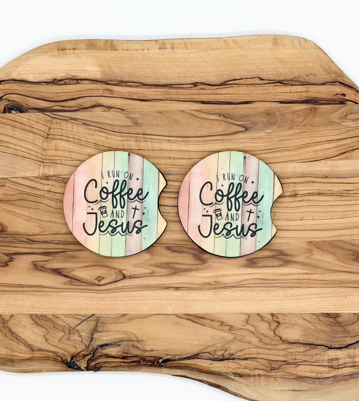 Two round coasters with a pastel wood-plank design and the text 'Run on Coffee and Jesus' laid on a large wooden serving board.